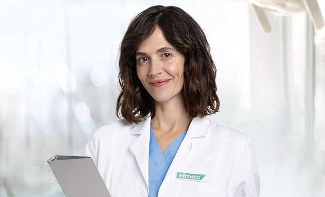 Odborník na ústní hygienu v bílém plášti před zeleným pozadím.